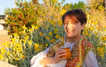 A woman smiles while drinking traditional mate among yellow flowers in Montevideo.