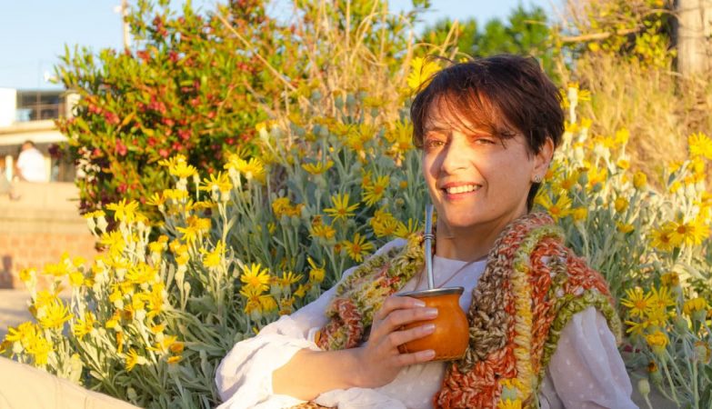 A woman smiles while drinking traditional mate among yellow flowers in Montevideo.