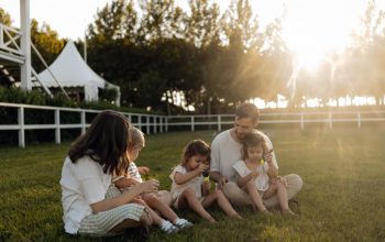 Family sitting on grass enjoying leisure time outdoors, with sun setting in the background.