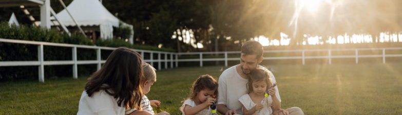 Family sitting on grass enjoying leisure time outdoors, with sun setting in the background.