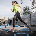 woman in green tank top and black leggings doing yoga on blue round trampoline