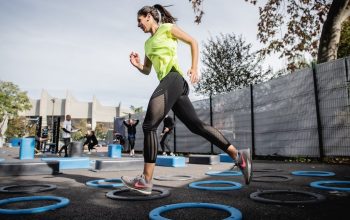 woman in green tank top and black leggings doing yoga on blue round trampoline