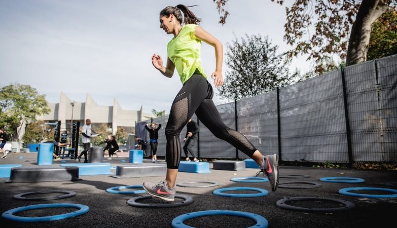 woman in green tank top and black leggings doing yoga on blue round trampoline